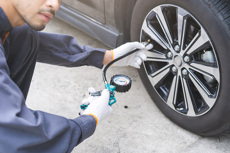 Technician checking GMC tire pressure for summer maintenance at Dunn Country GMC in Eufaula, OK