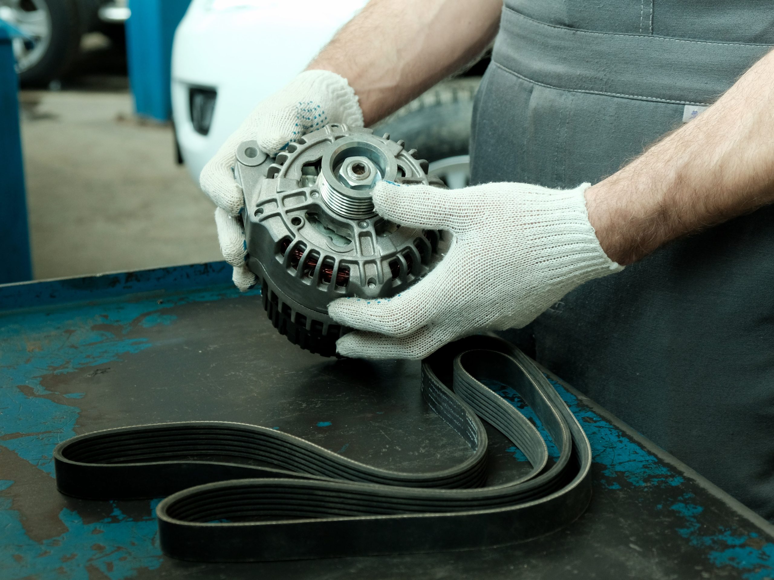 Mechanic holding an alternator next to a serpentine belt.